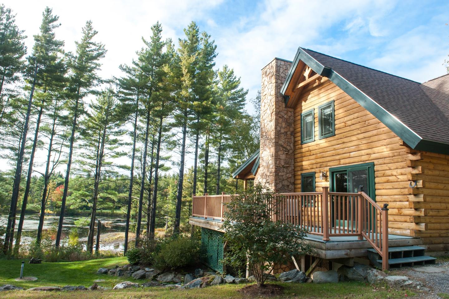 A log cabin at Sterling Ridge Resort overlooking a pond, framed by tall pines in Jeffersonville, Vermont